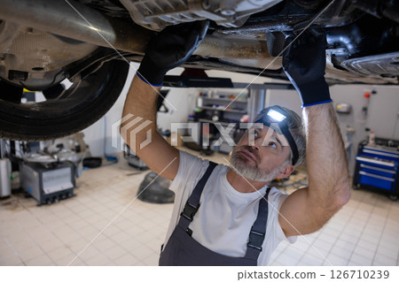 Mechanic inspecting undercarriage with headlamp Mechanic inspecting undercarriage with headlamp 126710239