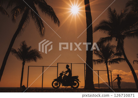 Silhouette of a Vietnamese man on a motorcycle on the embankment with palm trees by the sea at sunrise on summer morning in Vietnam Silhouette of a Vietnamese man on a motorcycle on the embankment with palm trees by the sea at sunrise on summer morning in Vietnam 126710871