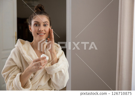 Trendy woman in robe practices personal facial care using gentle cleanser and cosmetics Trendy woman in robe practices personal facial care using gentle cleanser and cosmetics 126710875
