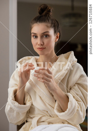 Cute woman with applies rejuvenating cream to her glowing face enjoying wellness 126710884