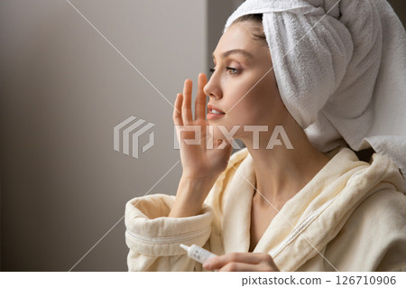 Beautiful woman in white robe gently applies natural facial cleanser to her skin Beautiful woman in white robe gently applies natural facial cleanser to her skin 126710906