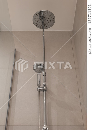 Upward view of chrome shower fixture with large round head and smaller handheld shower head Upward view of chrome shower fixture with large round head and smaller handheld shower head 126711591