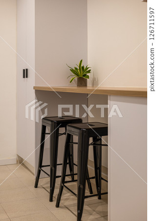 Kitchen bar area with wooden counter, two black bar stools and small potted plant on the surface 126711597