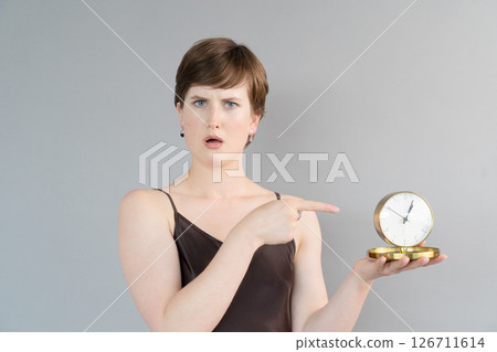 A Surprised Woman is Pointing at a Vintage Clock with a Look of Confusion on Her Face While Pondering 126711614