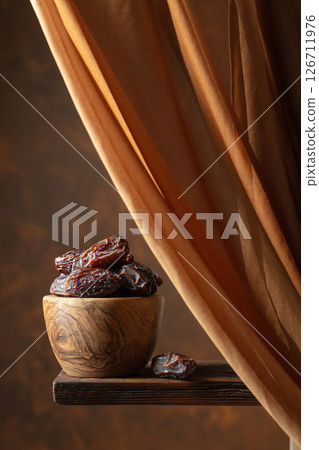 Dried medjool dates in wooden dish on a brown background. Dried medjool dates in wooden dish on a brown background. 126711976