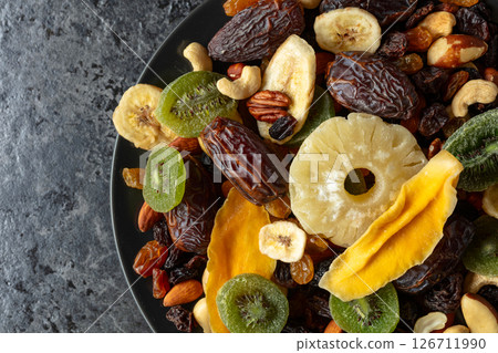 Dried tropical fruits, nuts, and raisins in black plate. Dried tropical fruits, nuts, and raisins in black plate. 126711990