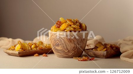Yellow sultana raisins in a wooden bowl on a beige background. 126712009
