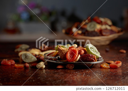 Dried tropical fruits, nuts, and raisins on a kitchen table. 126712011
