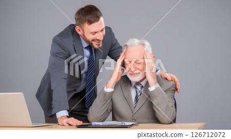 An older businessman struggling with pressure and a younger colleague supporting him, highlighting mental health in the corporate world 126712072