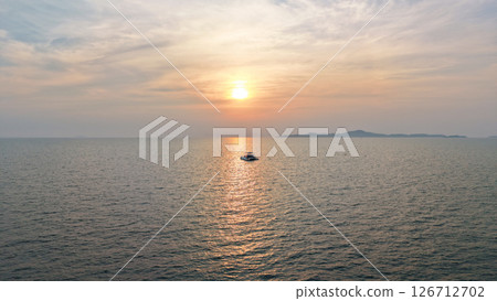 Catamaran sailing towards sunset over calm ocean with island in background Catamaran sailing towards sunset over calm ocean with island in background 126712702
