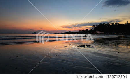 Vibrant sunset reflecting on wet sand with yacht sailing on calm sea 126712704