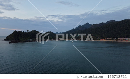 Tropical beach sunset illuminating clouds over distant mountains Tropical beach sunset illuminating clouds over distant mountains 126712711