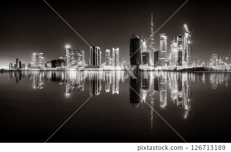 Urban city skyline with illuminated skyscrapers and waterfront railing in black and white at night, Dubai Marina bay UAE 126713189