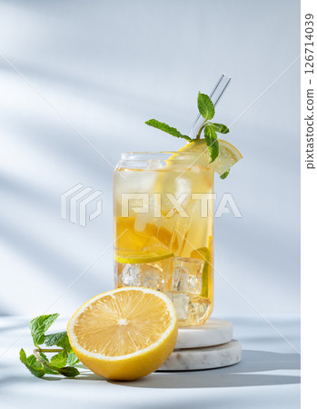 Iced drink with lemon and mint in a glass on a marble stand on light background with sunlight Iced drink with lemon and mint in a glass on a marble stand on light background with sunlight 126714039