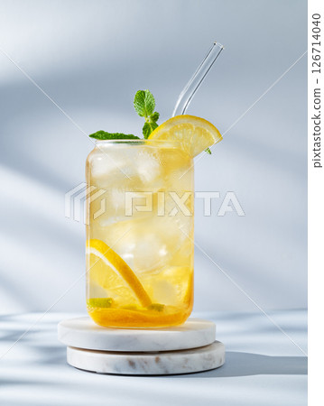 Iced drink with lemon and mint in a glass on a marble stand on light background with sunlight 126714040