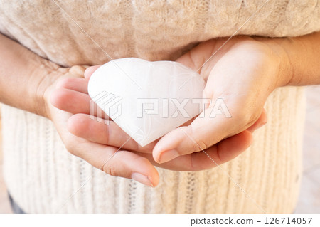 Womans hands holding heart made of stone crystal with flower of life pattern 126714057