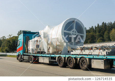 Long heavy industrial truck semi trailer platform transport disassembled wind turbine component wrapped plastic common highway on bright summer day. Energy industry equipment transportation service 126714535
