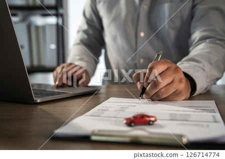 Insurance on paperwork assurance person gray shirt signing document with pen, small red toy car paper, and laptop desk, indicating business Insurance on paperwork assurance person gray shirt signing document with pen, small red toy car paper, and laptop desk, indicating business 126714774