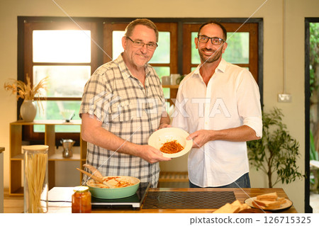 Elderly father and adult son presenting their finished meal in a warm home kitchen. Fathers day concept Elderly father and adult son presenting their finished meal in a warm home kitchen. Fathers day concept 126715325