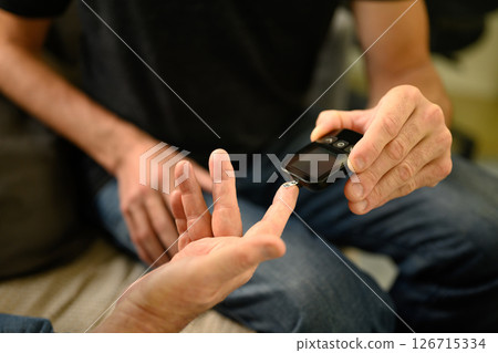 Son helping elderly father check blood sugar levels at home using a glucose meter. Fathers day concept. Son helping elderly father check blood sugar levels at home using a glucose meter. Fathers day concept. 126715334