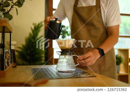Man pouring hot water into a coffee dripper, enjoying a mindful morning routine 126715362
