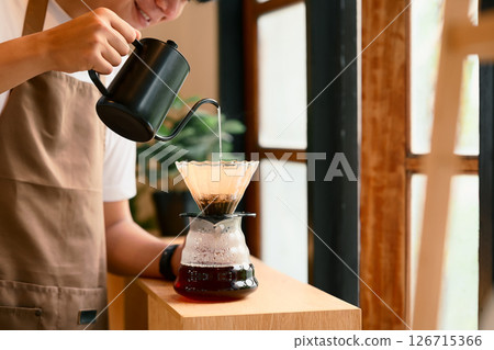Young man in apron brewing coffee using the pour-over method in warm kitchen 126715366