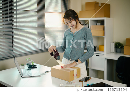 Young small business owner packing products for shipping in her home office 126715394