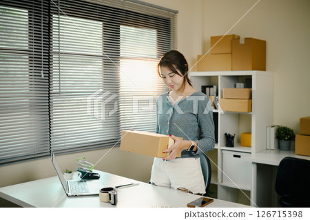 Small business owner handing over a packed parcel standing at her in home office Small business owner handing over a packed parcel standing at her in home office 126715398