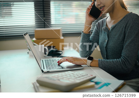 Young woman business owner communicating with client and checking inventory on laptop Young woman business owner communicating with client and checking inventory on laptop 126715399
