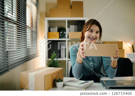 Smiling female entrepreneur holding a package preparing a product for shipment Smiling female entrepreneur holding a package preparing a product for shipment 126715400