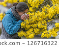 A woman in a blue jacket wipes her nose amidst vibrant yellow flowers on a rainy day 126716322