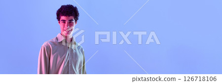 Banner. Smiling curly-haired boy in relaxed pose, dressed shirt, in neon light against background with negative space 126718106
