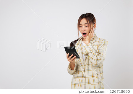 Holding a calculator tightly, woman shows a shocked reaction while checking the calculator again, facing accounting confusion and financial concerns. isolated studio white background, Tax day concept Holding a calculator tightly, woman shows a shocked reaction while checking the calculator again, facing accounting confusion and financial concerns. isolated studio white background, Tax day concept 126718690