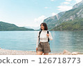 Lost in the moment, a happy woman hikes a quiet path between green hills, the lake glinting nearby and the mountains rising like a dream 126718773