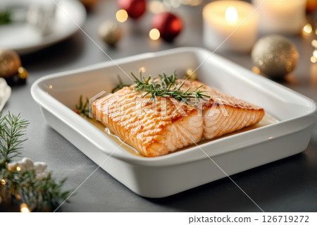Delicious baked salmon fillet garnished with fresh dill and spices, served in a ceramic dish. Festive holiday setting with candles and elegant table decor in soft focus. Copy space. Banner 126719272