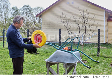 Unpacking new wheel and preparing for replacement of damaged tire on garden wheelbarrow to ensure smooth transport of heavy loads. Unpacking new wheel and preparing for replacement of damaged tire on garden wheelbarrow to ensure smooth transport of heavy loads. 126719534