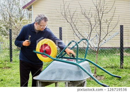 Gardener installing flat free wheel on garden cart to enhance durability and prevent punctures during outdoor tasks. Gardener installing flat free wheel on garden cart to enhance durability and prevent punctures during outdoor tasks. 126719536