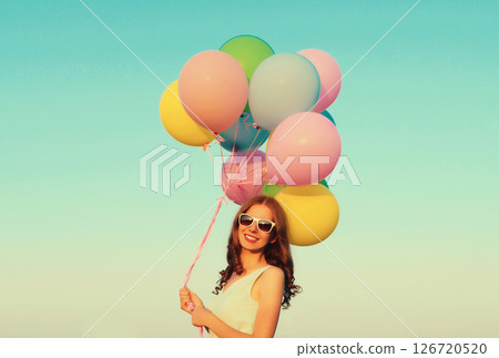 Happy smiling young woman with bunch of colorful balloons outdoors against sky background Happy smiling young woman with bunch of colorful balloons outdoors against sky background 126720520