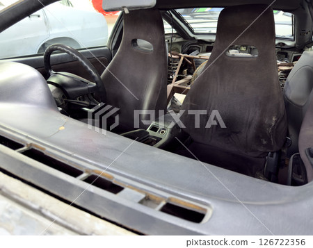Old sport car interior with worn bucket seats, stripped rear section and roll cage installation, showcasing restoration stage before final rebuild and customization Old sport car interior with worn bucket seats, stripped rear section and roll cage installation, showcasing restoration stage before final rebuild and customization 126722356