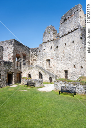 Visitors enjoy the vibrant green courtyard of Rabi Castle, surrounded by ancient stone walls. The sunny day offers a perfect setting for exploration and relaxation among ruins. 126722559