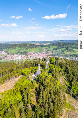 Svatobor Lookout Tower rises prominently over the valley, offering a stunning aerial view of Susice town and the surrounding green landscape. This vantage point showcases the beauty of the region. Svatobor Lookout Tower rises prominently over the valley, offering a stunning aerial view of Susice town and the surrounding green landscape. This vantage point showcases the beauty of the region. 126722562