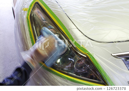 After protecting the paintwork of the body with masking tape, the headlight surface that has yellowed due to aging is being polished. After protecting the paintwork of the body with masking tape, the headlight surface that has yellowed due to aging is being polished. 126723378