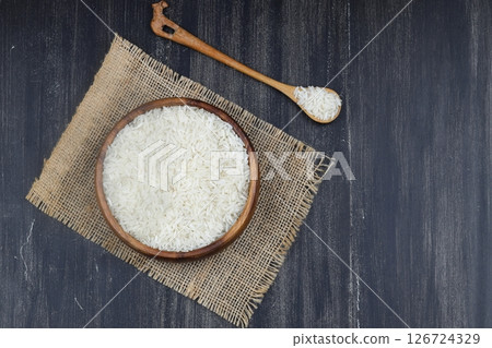 Raw white rice on wooden background. Long uncooked rice in wooden plate. Natural organic food. Traditional Asian cereal culture. 126724329