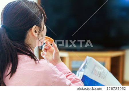 一位女士一邊吃零食一邊看電視 126725962