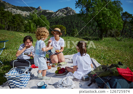 A family gathers on a blanket amidst beautiful mountain nature, enjoying a sunny day with food and joyful interaction, symbolizing togetherness, relaxation, and the beauty of outdoor recreation. A family gathers on a blanket amidst beautiful mountain nature, enjoying a sunny day with food and joyful interaction, symbolizing togetherness, relaxation, and the beauty of outdoor recreation. 126725974