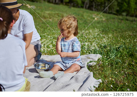 A mother and her children enjoy a lovely picnic surrounded by picturesque mountain scenery, celebrating time together in nature. 126725975