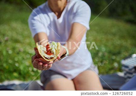 A mother enjoys quality family time during a relaxing picnic in the mountains, presenting a delicious taco in the foreground amidst the serene natural surroundings. 126726052