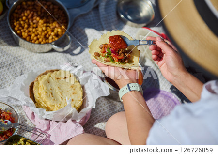 A family enjoying a picnic in nature, preparing tacos with fresh ingredients, celebrating togetherness and enjoying the outdoors during a bright summer day. 126726059