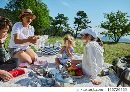 Family Enjoying a Relaxing Picnic in Scenic Mountain Landscape on a Warm, Sunny Day Family Enjoying a Relaxing Picnic in Scenic Mountain Landscape on a Warm, Sunny Day 126726363