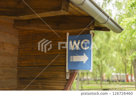 A blue sign indicates the direction of restroom facilities with a clear arrow pointing right. The sign is mounted on a wooden structure in a serene outdoor setting 126726460